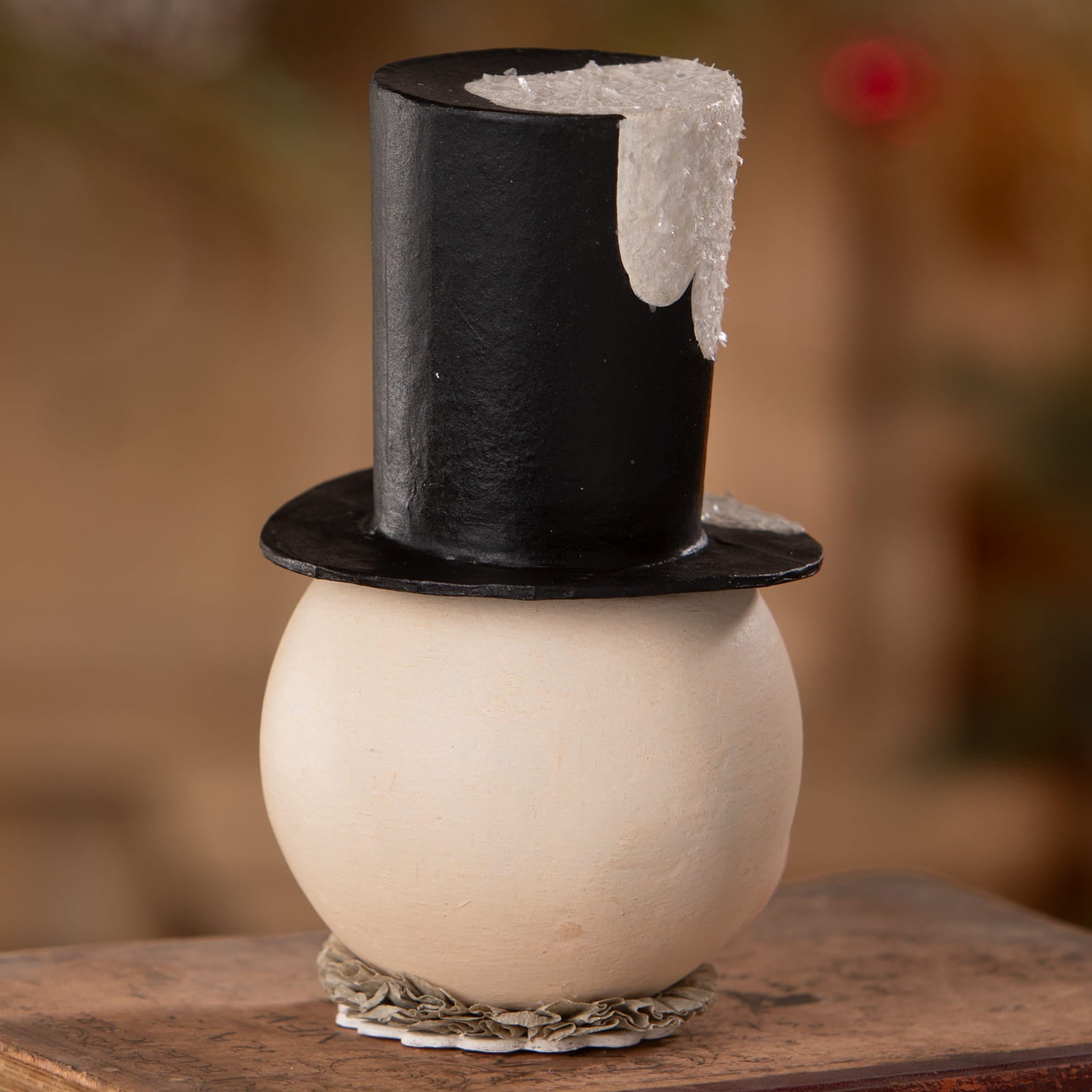 A cream jolly bobble snowman container with a glossy black top hat and ruffled base perfect for christmas snowman decor