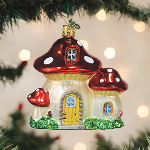 A charming red and white mushroom house ornament made of glass with a yellow door hanging on a christmas tree