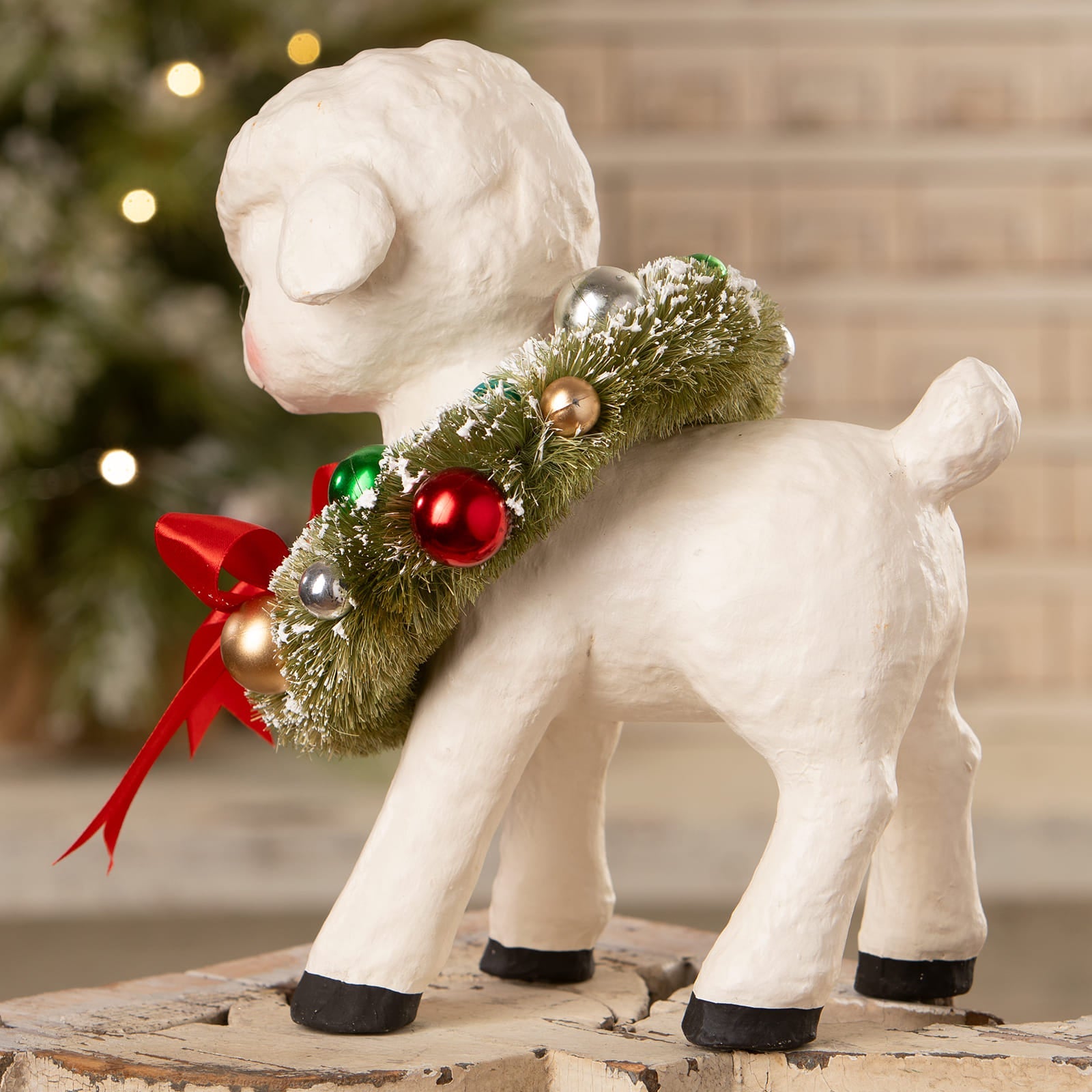 White ceramic noelle lamb with wreath featuring green frosted greenery and red gold silver ornaments by bethany lowe design