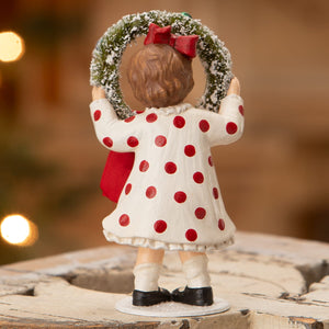 A bethany lowe design noelle figurine with white polka dots holding a green wreath with snow texture and red bow