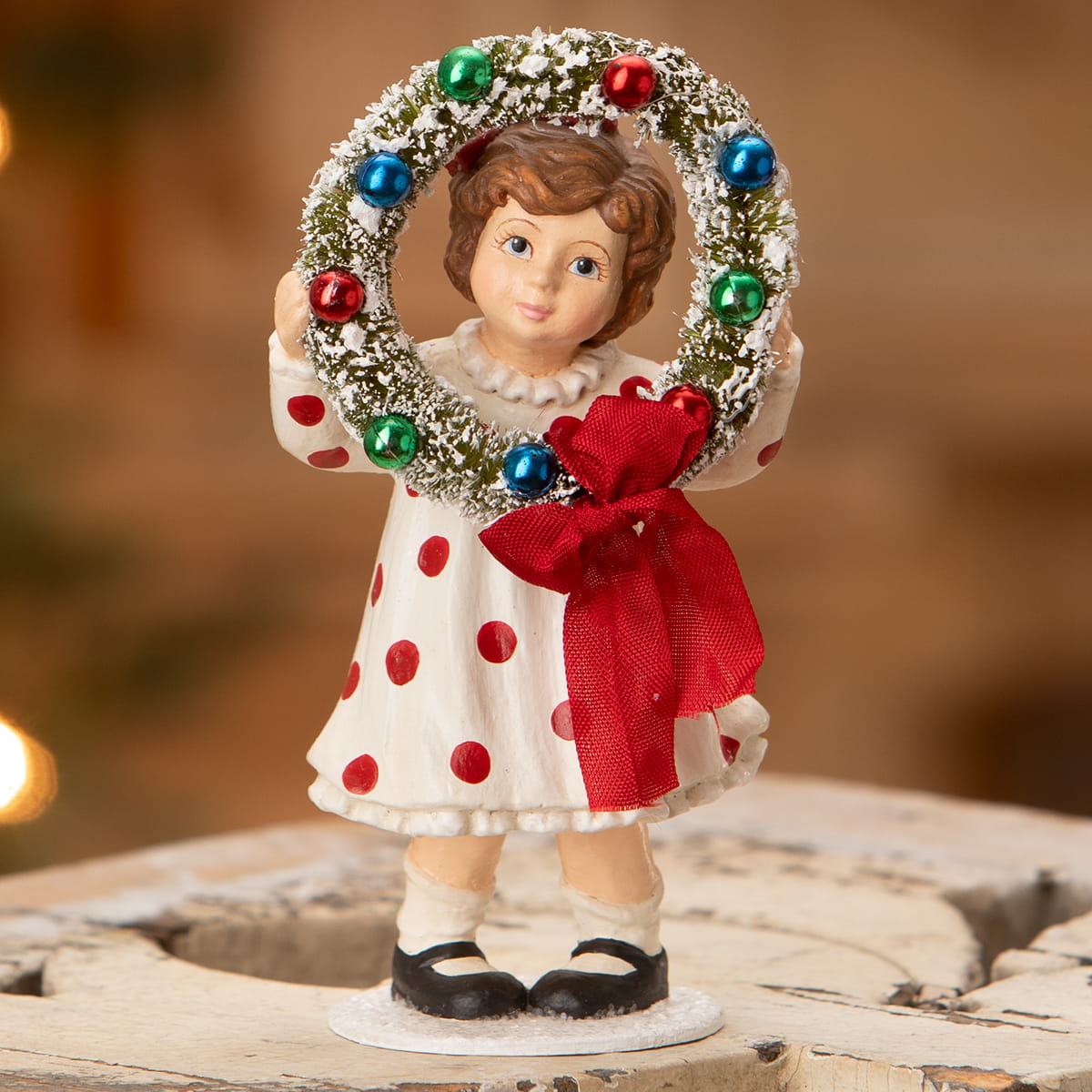 A bethany lowe design porcelain figurine named noelle holding a wreath with greenery and colorful ornaments