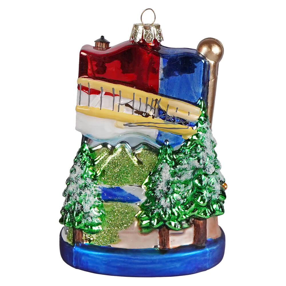 Vibrant north carolina glass ornament featuring a red and blue building with a yellow plane over snowy pine trees