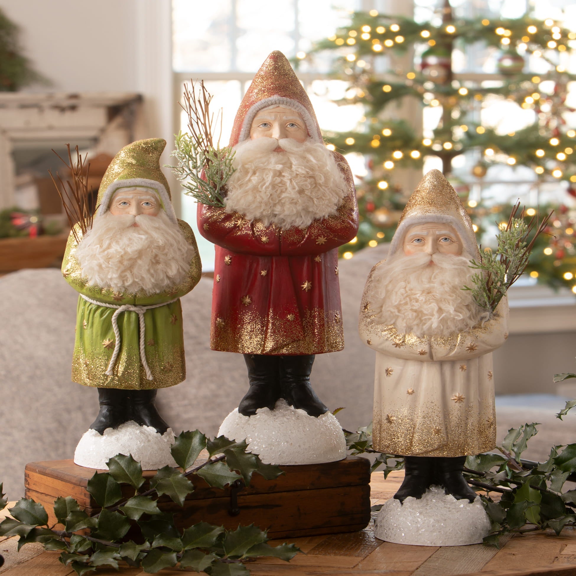 Three glittery nostalgic winter belsnickle santa figurines with white beards holding greenery spreading holiday cheer