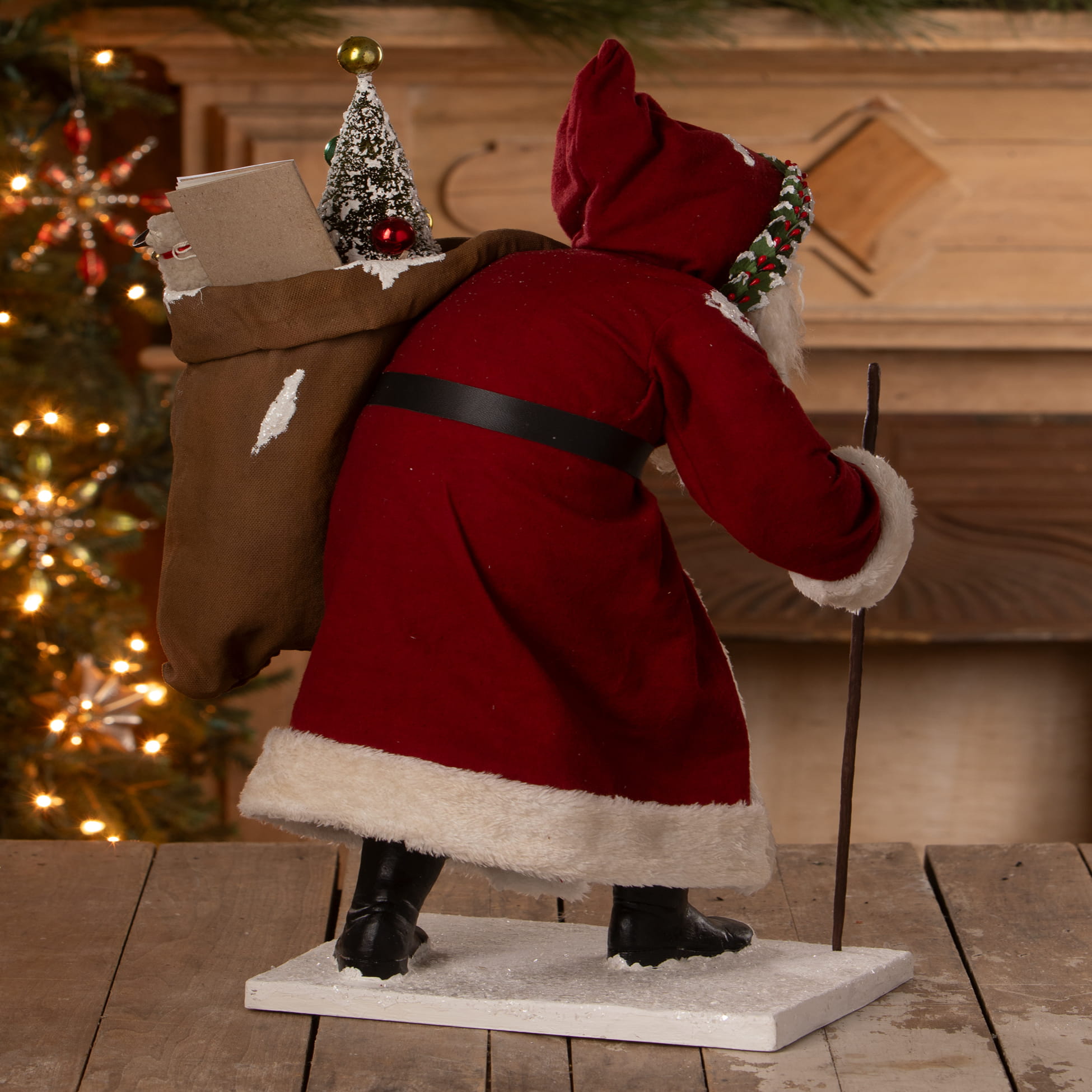 Old st nick santa figure in red with white fur trim black belt boots carrying bag of toys with snow-covered tree by bethany lowe designs