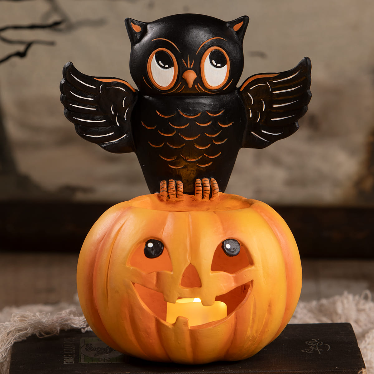 Black owl figurine with orange accents perched on glowing orange halloween pumpkin lantern for spooky decor