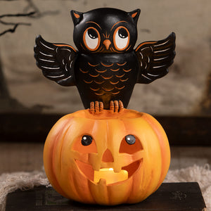 Black owl figurine with orange accents perched on glowing orange halloween pumpkin lantern for spooky decor