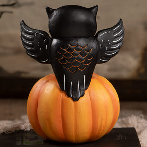 Black owl figurine with white-lined wings and orange-scaled back perched on an orange halloween pumpkin