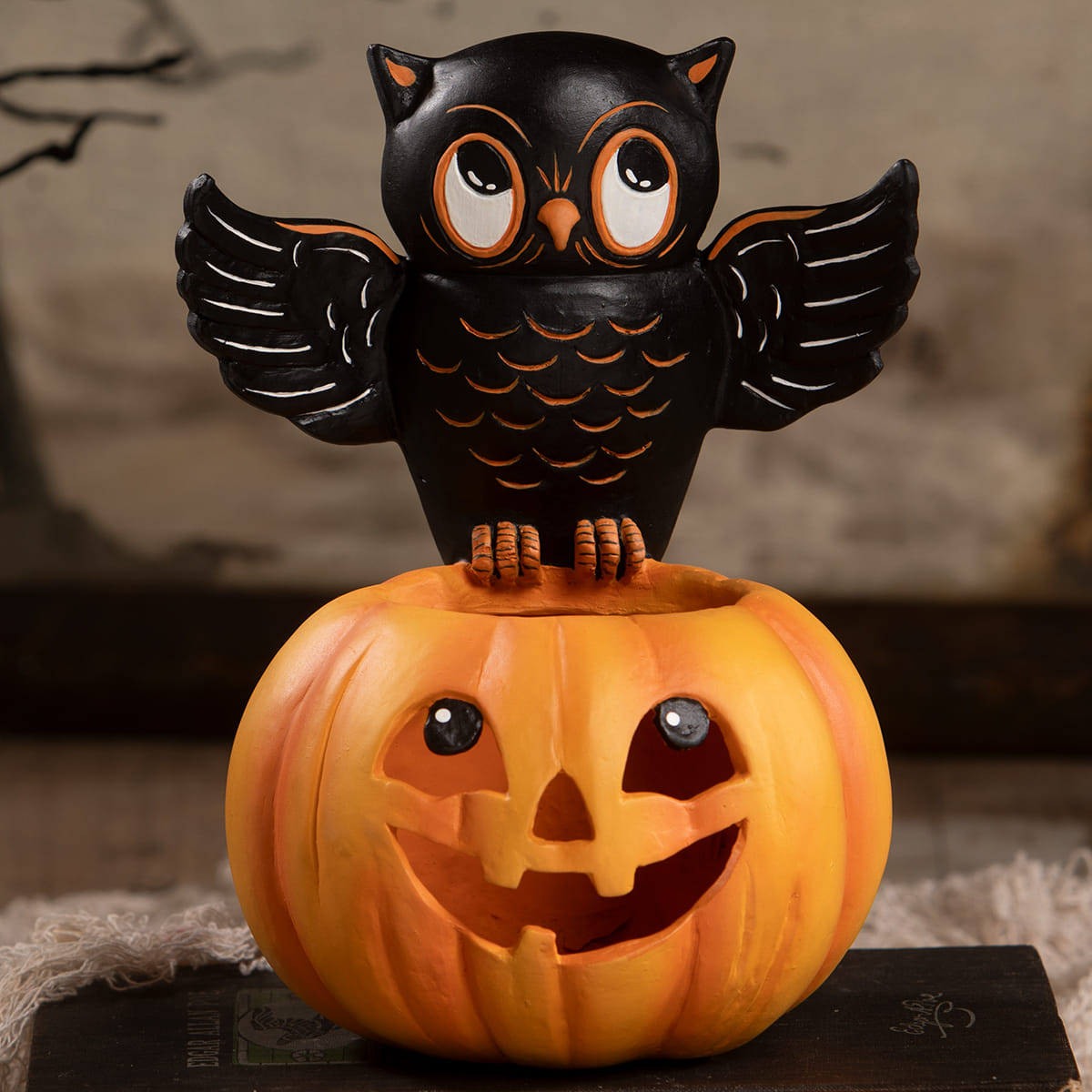 Black owl figurine with orange accents perched on a carved orange halloween pumpkin for seasonal decor