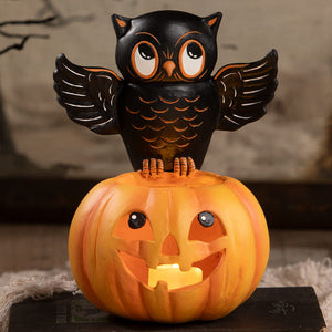 Black owl figurine with orange accents perched on a glowing halloween pumpkin lantern for halloween pumpkins and gourds decor