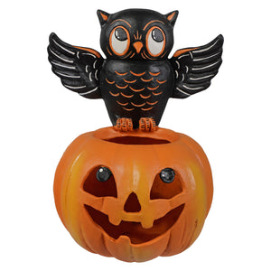 Black owl with orange accents perched on an orange jack o lantern halloween pumpkin container
