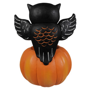 Black owl figurine with white wing outlines and orange scalloped details perched on halloween pumpkins and gourds