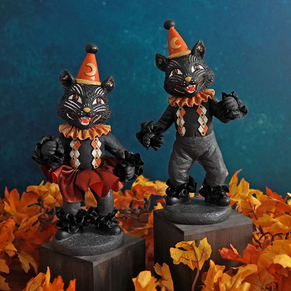 Two vintage-style Halloween cat figurines wearing orange party hats and clown-like costumes.