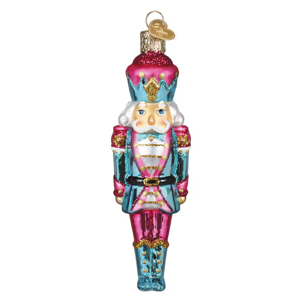 A vibrant pink and teal glass pastel nutcracker ornament with gold accents and glittery crown for figural decor or tabletop decor