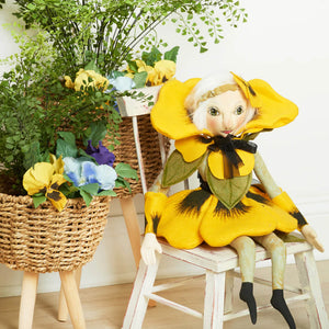 A charming yellow felt paulina pansy flower doll with green leaf accents and black ribbon bow seated on white chair gallerie ii design family owned