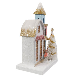 A petite light blue house church with glittery snow roofs, pink awnings, a white tree, and a small deer figurine nearby