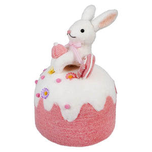 White plush bunny sitting atop a pink and white decorated cake-shaped ornament.