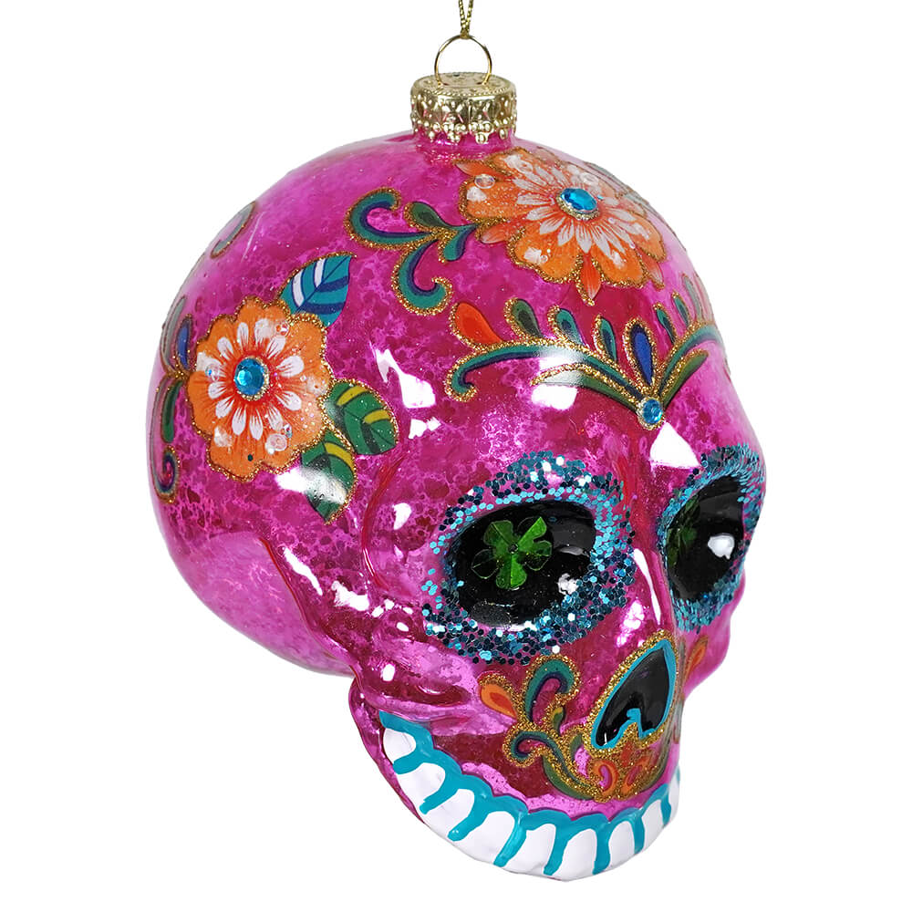 Vibrantly decorated pink glass sugar skull ornament with floral patterns and glitter accents for dia de los muertos