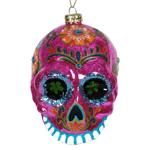 Vibrant pink glass sugar skull ornament with glittery blue eyes and colorful floral accents perfect as dia de los muertos ornament