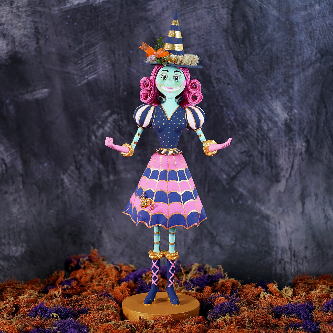 A whimsical itchy witchy figurine in pink and navy with gold accents and a striped hat for halloween witch decor