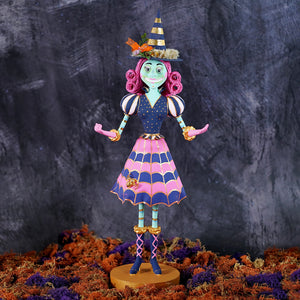 A whimsical itchy witchy figurine in pink and navy with gold accents and a striped hat for halloween witch decor