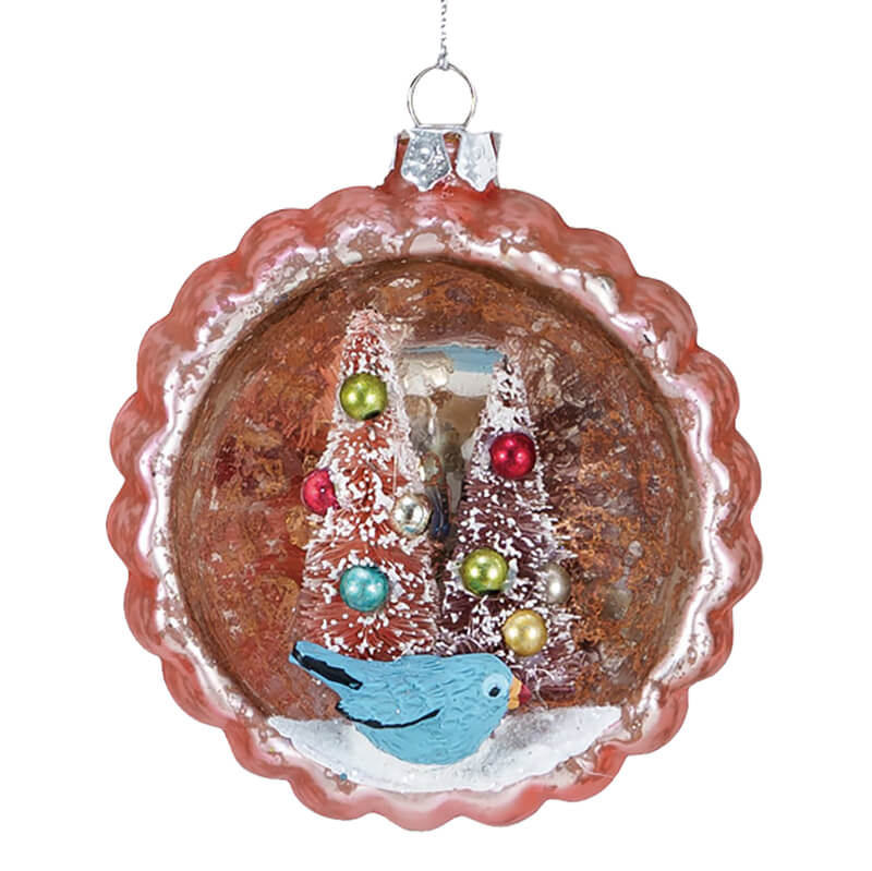 Christmas tree ornament depicting a winter scene with decorated trees and a blue bird.