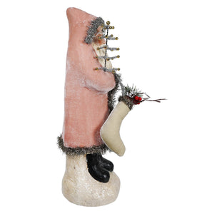 Pink velvet belsnickle figurine with silver tinsel trim and gold buttons holding cream stocking with red berries