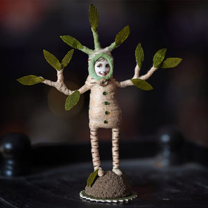 Whimsical beige felt plant person figure with green paper leaves standing on a miniature woodland mound