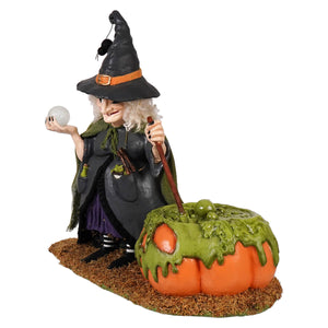 A detailed poison brewing pruella figurine of a witch in a black hat holding a white orb beside a pumpkin cauldron