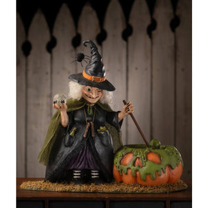 A whimsical poison brewing pruella witch figurine with black hat orange band spider dark green cape and pumpkin decoration