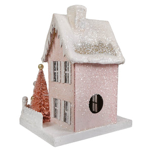 Pink glittery bethany lowe pink cottage ornament with snowy roof and copper tree beside light cord attachment