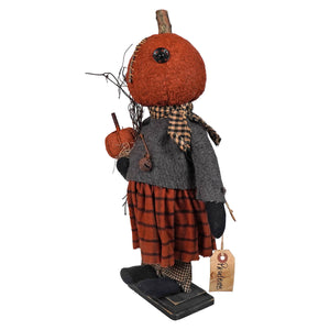 Whimsical pumpkin-headed doll figure wearing a plaid skirt and gray jacket.
