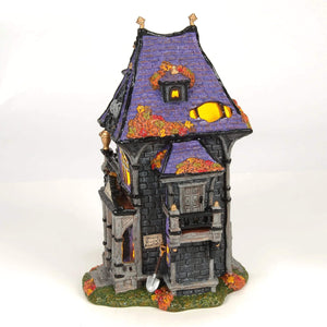 A miniature haunted house figurine with a purple roof and black stone walls from puckett’s funerarium with autumn leaves