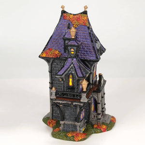 A miniature haunted house figurine with purple tiled roof and black stone walls surrounded by autumn leaves from puckett’s funerarium