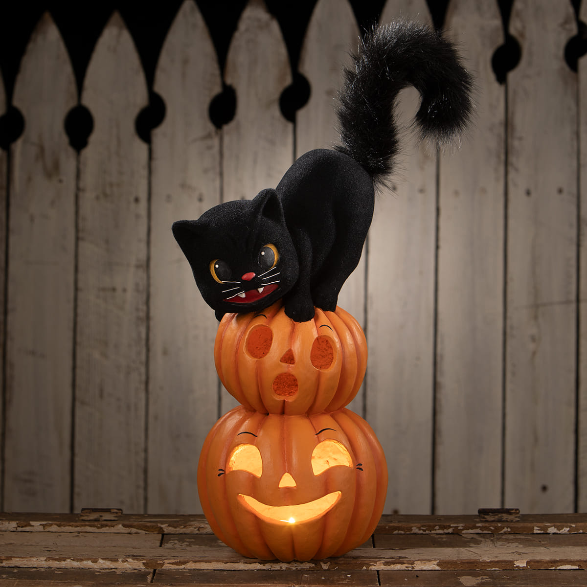 Black plush halloween cat perched on two stacked orange illuminated halloween pumpkins and gourds
