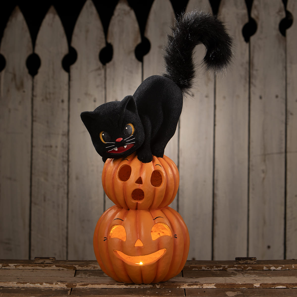 Black plush cat sitting on stacked orange halloween pumpkins with glowing faces perfect for halloween cats decor