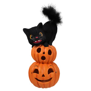 Black plush cat with fluffy tail perched on two stacked orange halloween pumpkins and gourds perfect for halloween cats decor