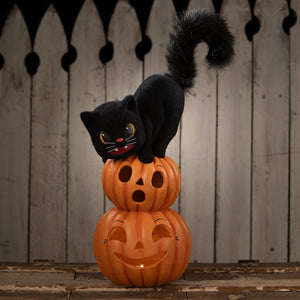 Black plush cat perched on stacked glowing orange halloween pumpkins with carved faces perfect for halloween cats decor