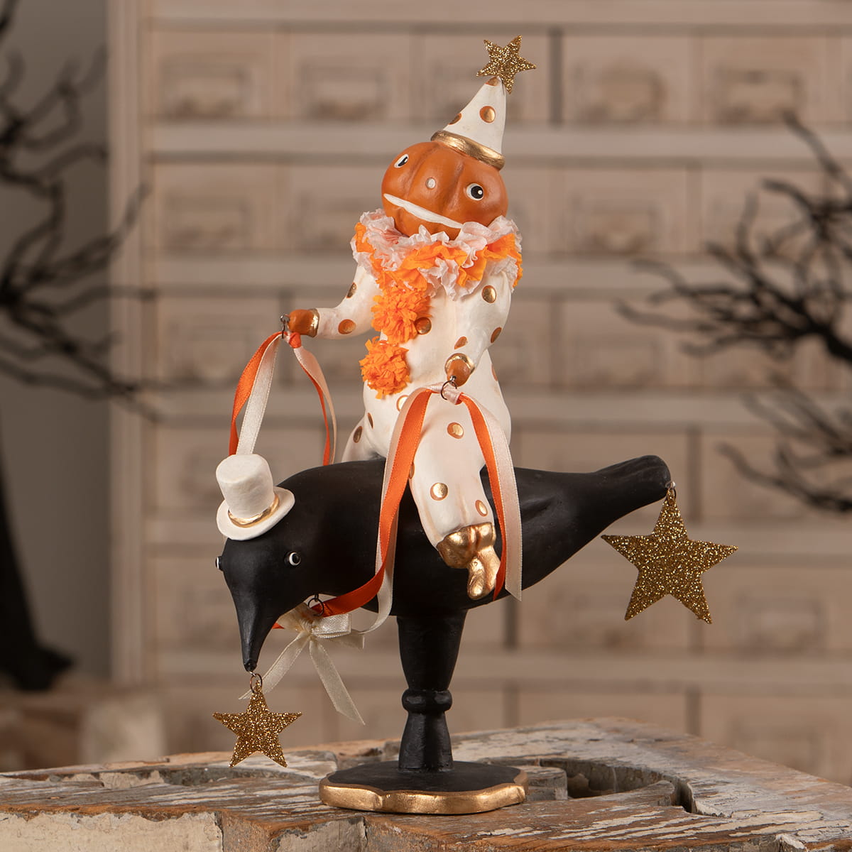 Ornamental figurine pumpkinhead on crow features a jack o lantern jester in orange polka dots riding a black crow