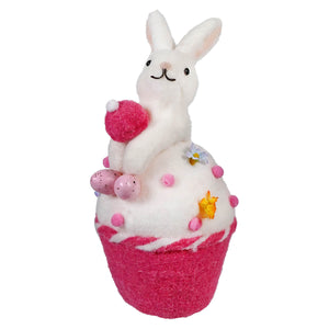 A white bunny sits atop a pink and white cupcake-shaped bath bomb decorated with stars and dots.