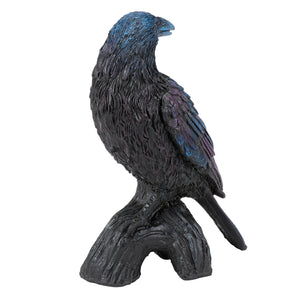 A glossy black and iridescent blue raven figurine with gothic charm perched on a textured tree branch base