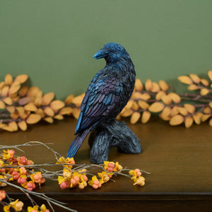 A glossy iridescent blue raven figurine with gothic charm perched on a dark textured branch base