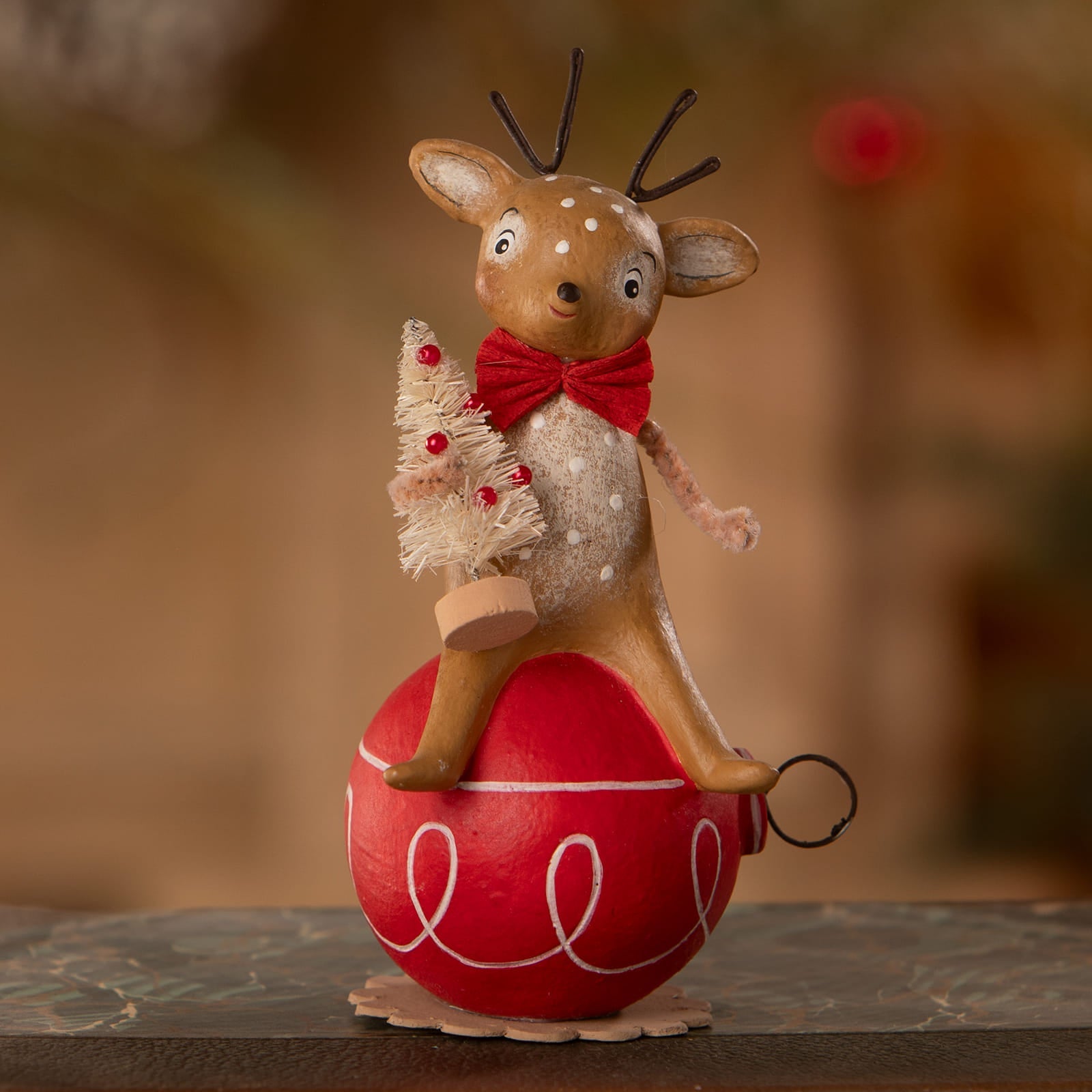 A charming brown reindeer figurine with white spots and red bow tie holding a frosted tree on a red ornament by bethany lowe designs christmas reindeer figures ornaments and decor