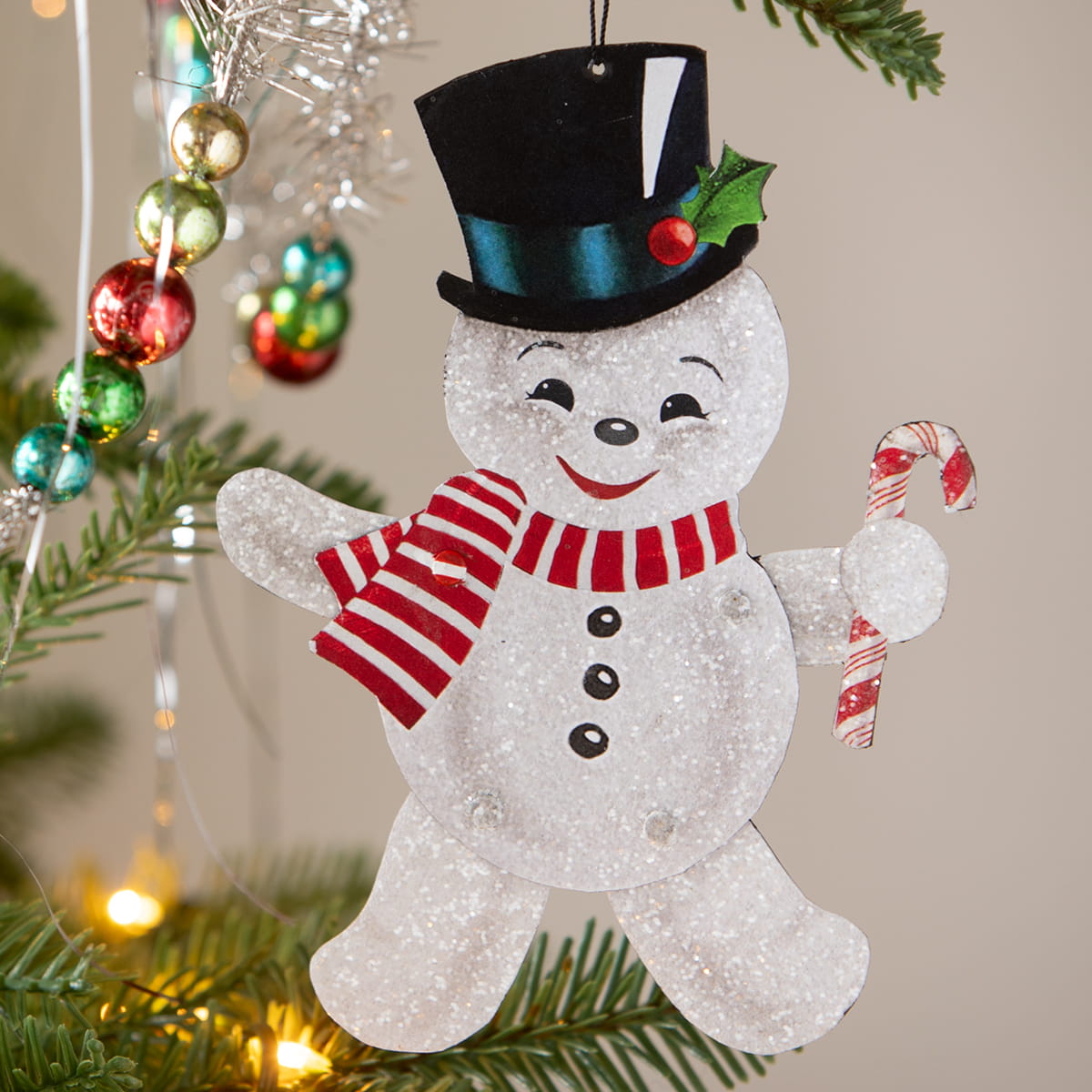 A glittery white bethany lowe design retro rockin snowman ornament with black top hat and candy cane accessory