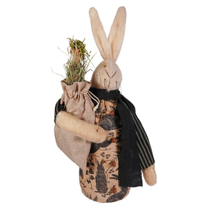 Beige fabric robin rabbit figurine with long ears wearing patterned apron and black scarf holding hay sack for decorative pillow