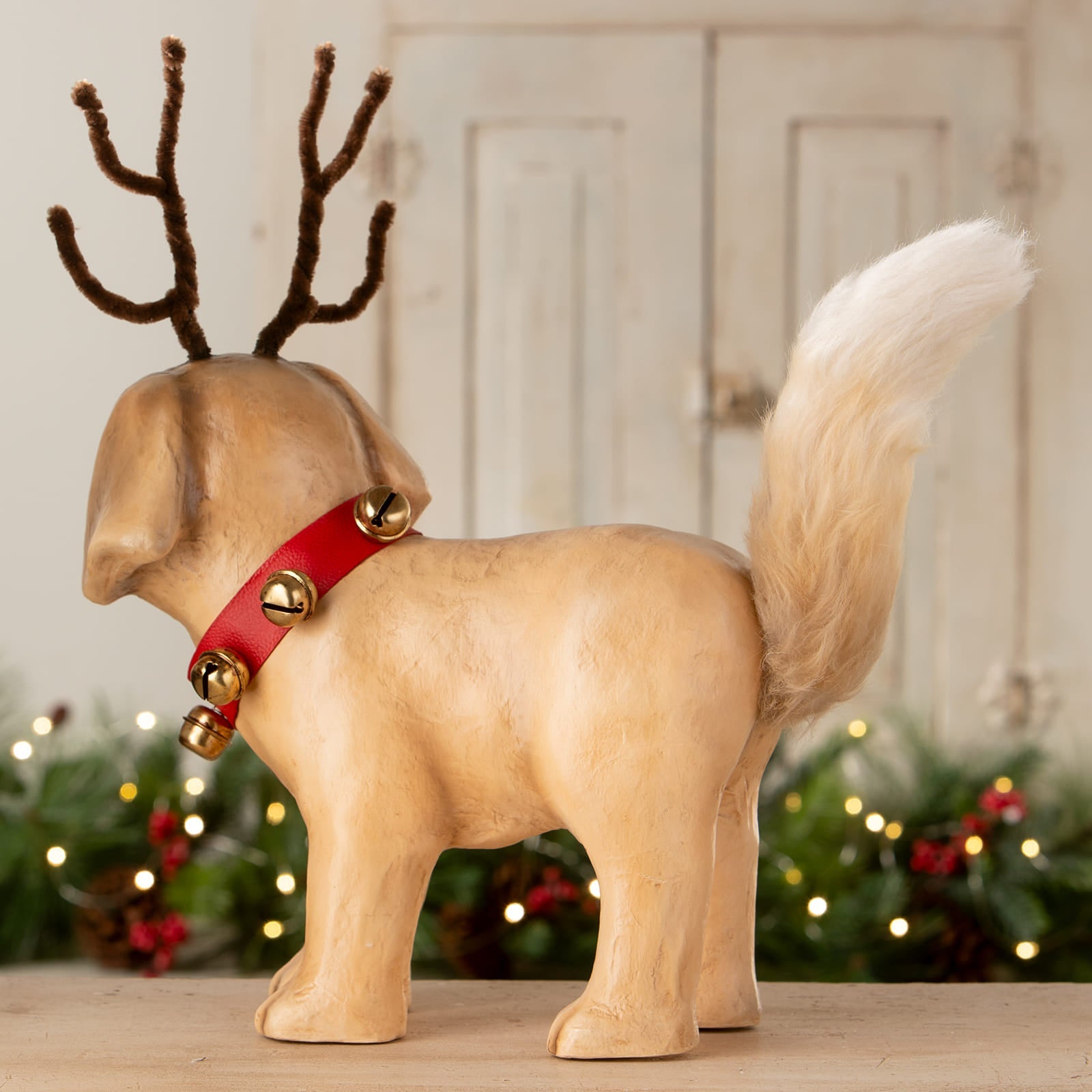 A beige ceramic rudolph puppy figurine by bethany lowe design with brown pipe-cleaner antlers and a red collar with gold bells