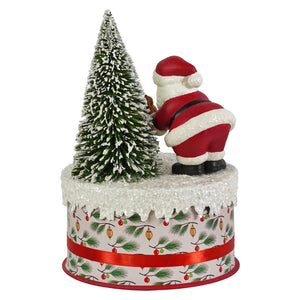 Red and white bethany lowe design santa figure placing snow-dusted tree on festive base in santa and deer on box decor