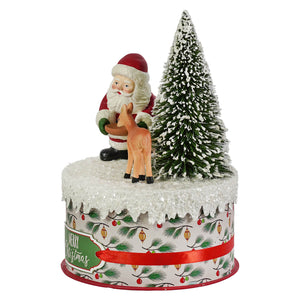 A bethany lowe design festive tin featuring a santa figure in red holding a christmas reindeer ornament on a snowy green tree