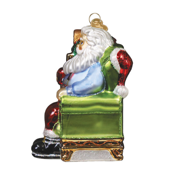 Glass santa ornament with white beard red and black suit blue shirt and gold glittery details on green chair