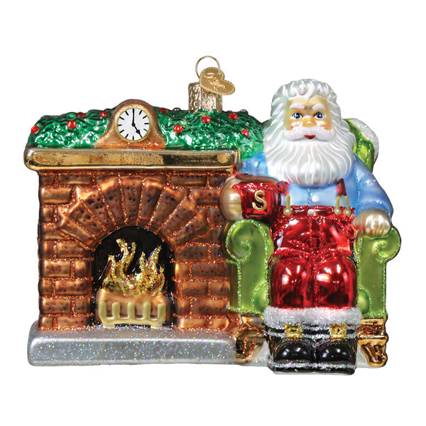 Glass santa ornament in red and blue with gold trim seated in green armchair by brick fireplace clock santa at hearth