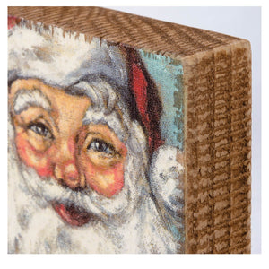 A rustic wooden santa block sign by kathy design featuring a painted santa with rosy cheeks and red hat